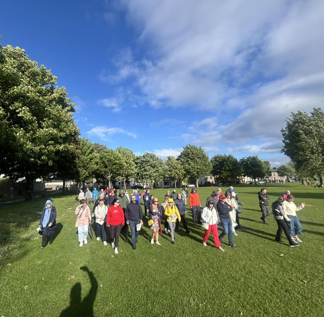 A group of people walking together across a green park under a blue sky