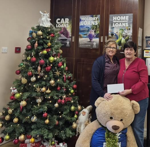 Two women holding an envelope next to a decorated Christmas tree